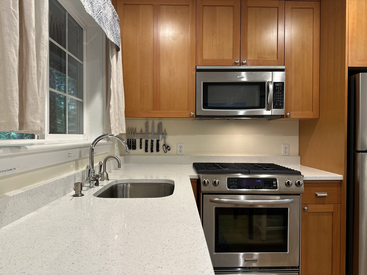 The kitchen: wood shaker cabinets, white counters, an undermount sink by the window, a gas range and a magnetic knife strip