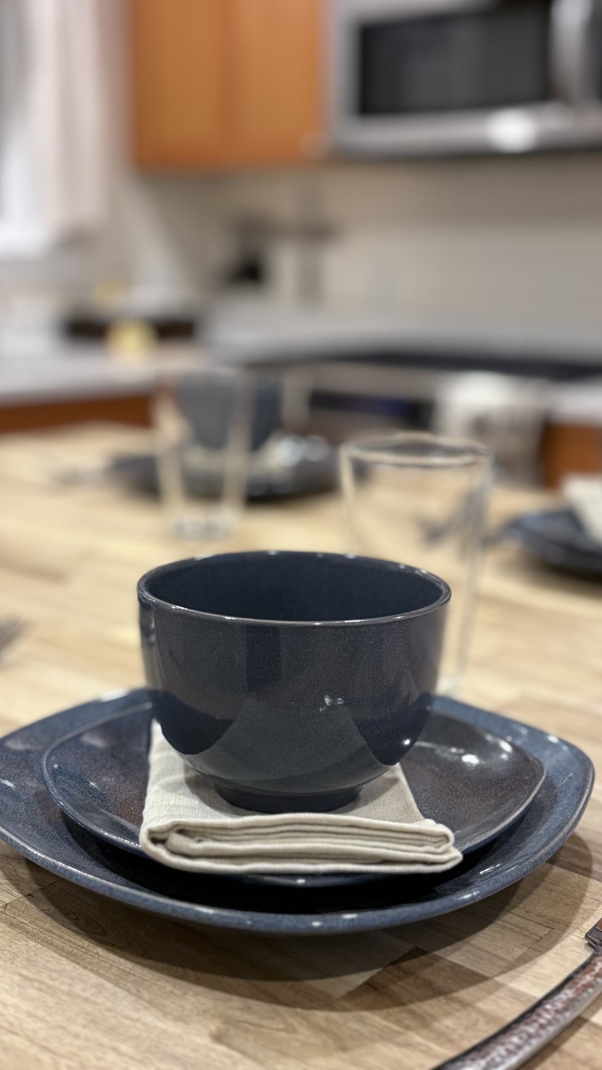 A place setting of blue stoneware and a linen napkin on the butcher-block table, with the kitchen behind