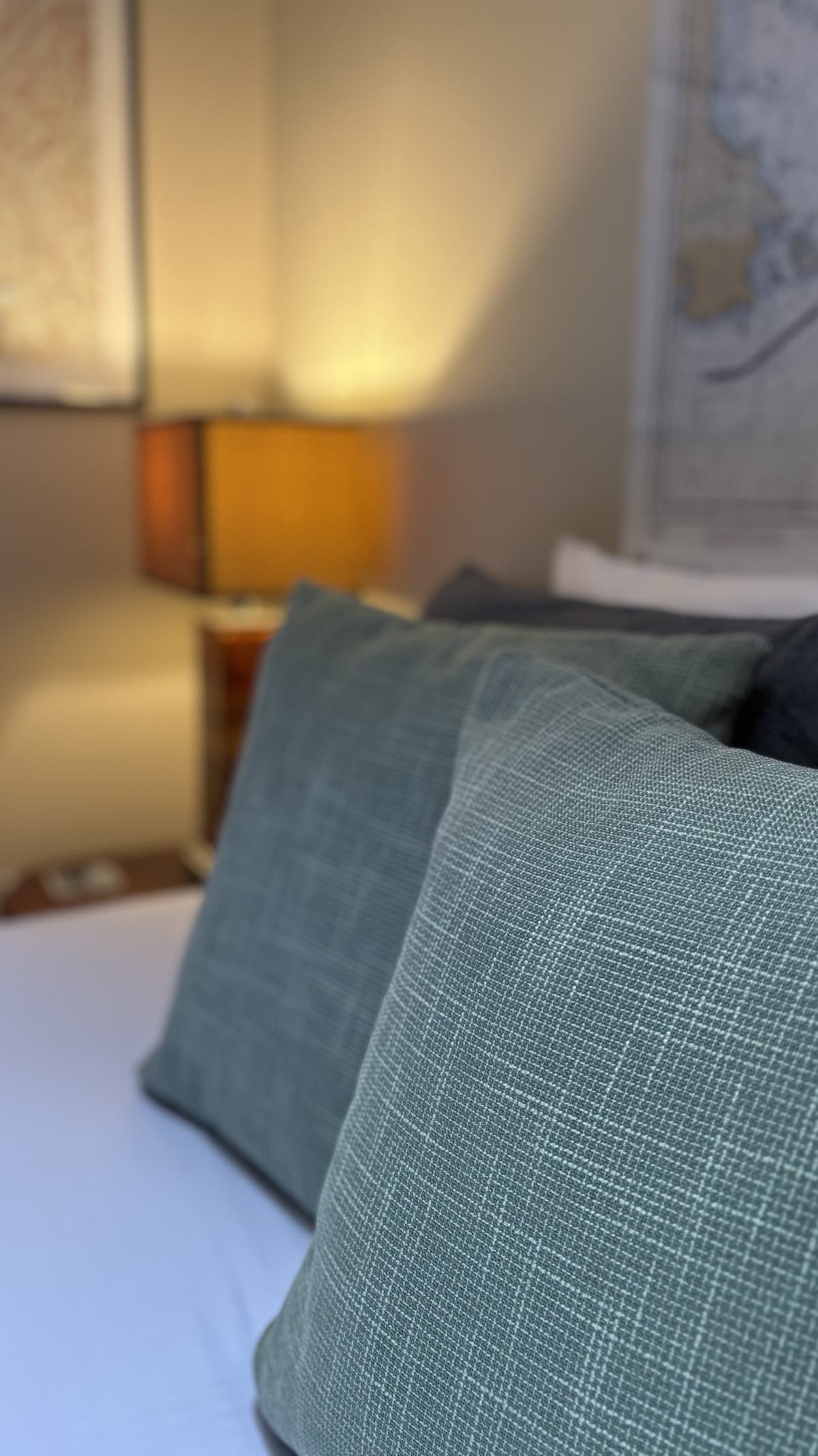 Close-up of textured teal throw pillows on the queen bed, with a warm lamp glowing softly behind