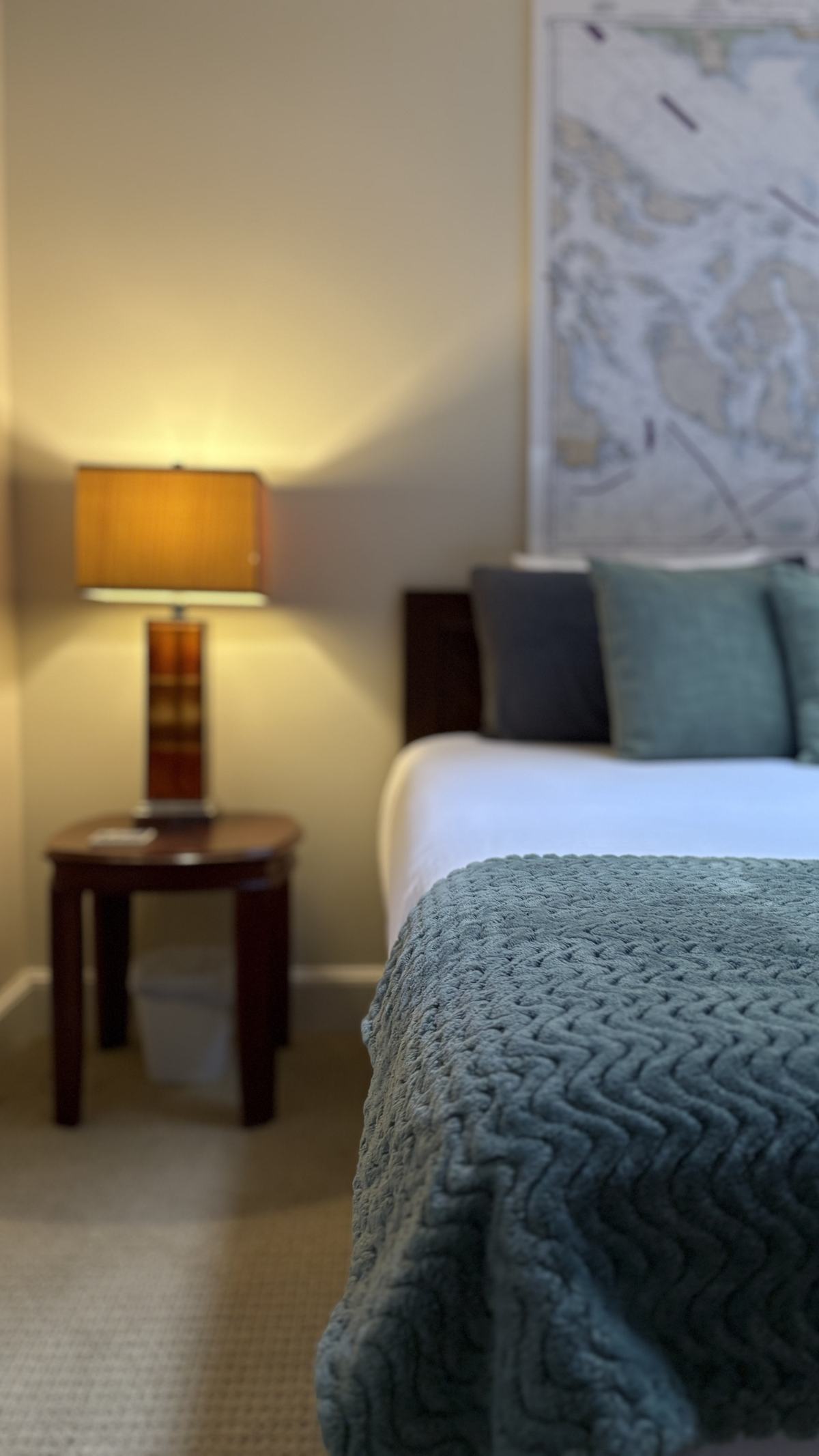 A teal chevron throw across the foot of the queen bed, with a lamp-lit nightstand softly out of focus