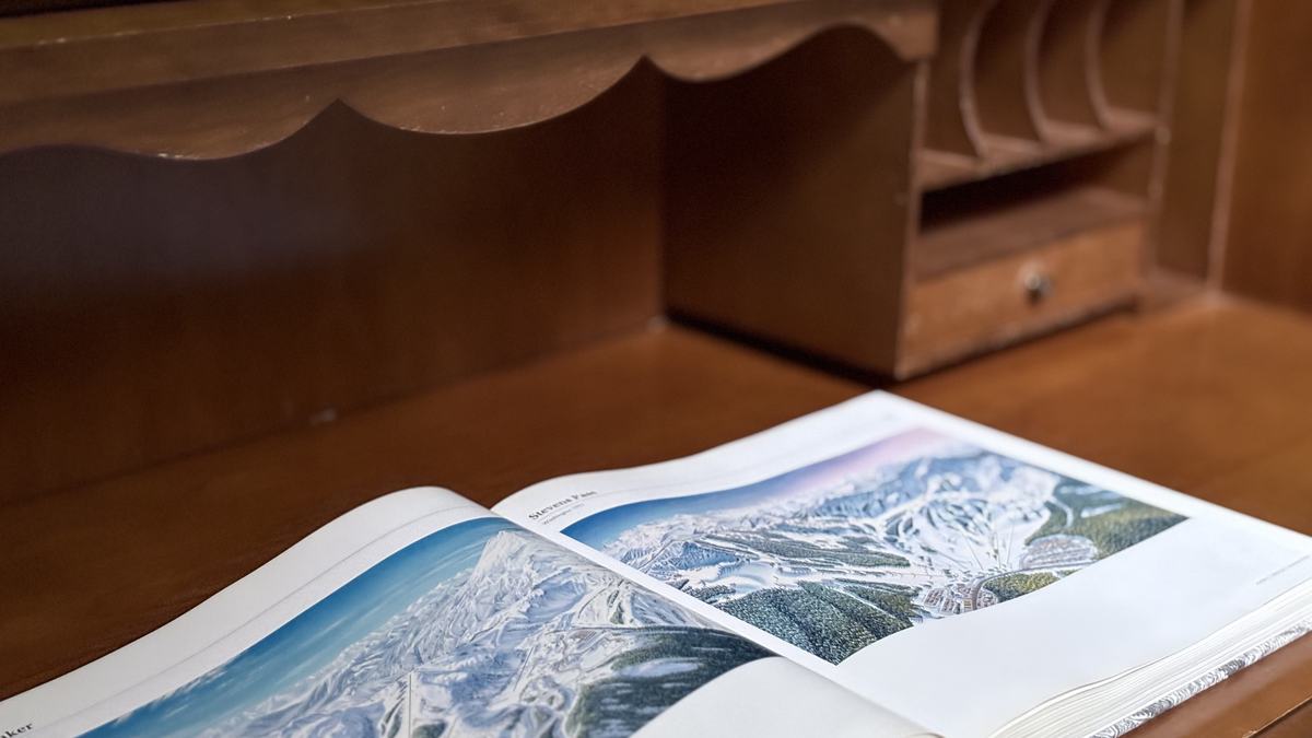 An open book of painted ski-area maps on the roll-top desk in the king suite